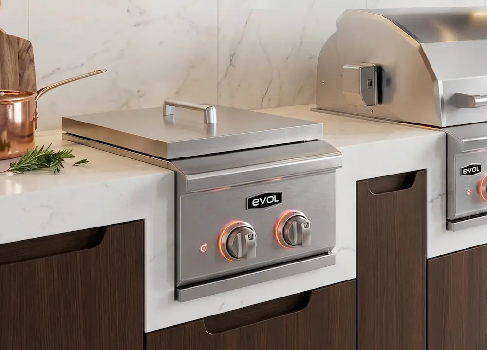 Side burner embutido em aço inox integrado à bancada de área gourmet planejada, com dois queimadores de alta potência, instalado ao lado de uma churrasqueira a gás Evol para preparo simultâneo de acompanhamentos e finalizações.
