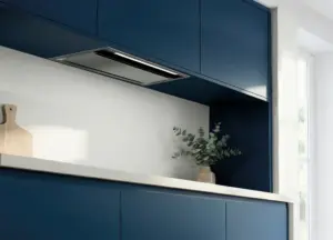Coifa de embutir Evol instalada em armário superior de cozinha planejada azul, com acabamento em aço inox, iluminação em LED e design discreto integrado à marcenaria contemporânea.