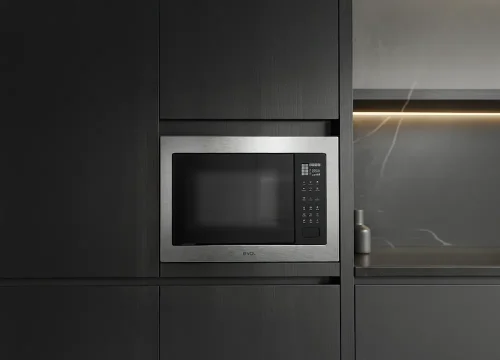 Micro-ondas de embutir em inox integrado à marcenaria escura de cozinha planejada contemporânea, com acabamento minimalista e iluminação indireta ao fundo.