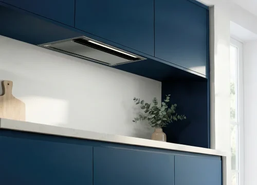 Coifa de embutir Evol instalada em armário superior de cozinha planejada azul, com acabamento em aço inox, iluminação em LED e design discreto integrado à marcenaria contemporânea.